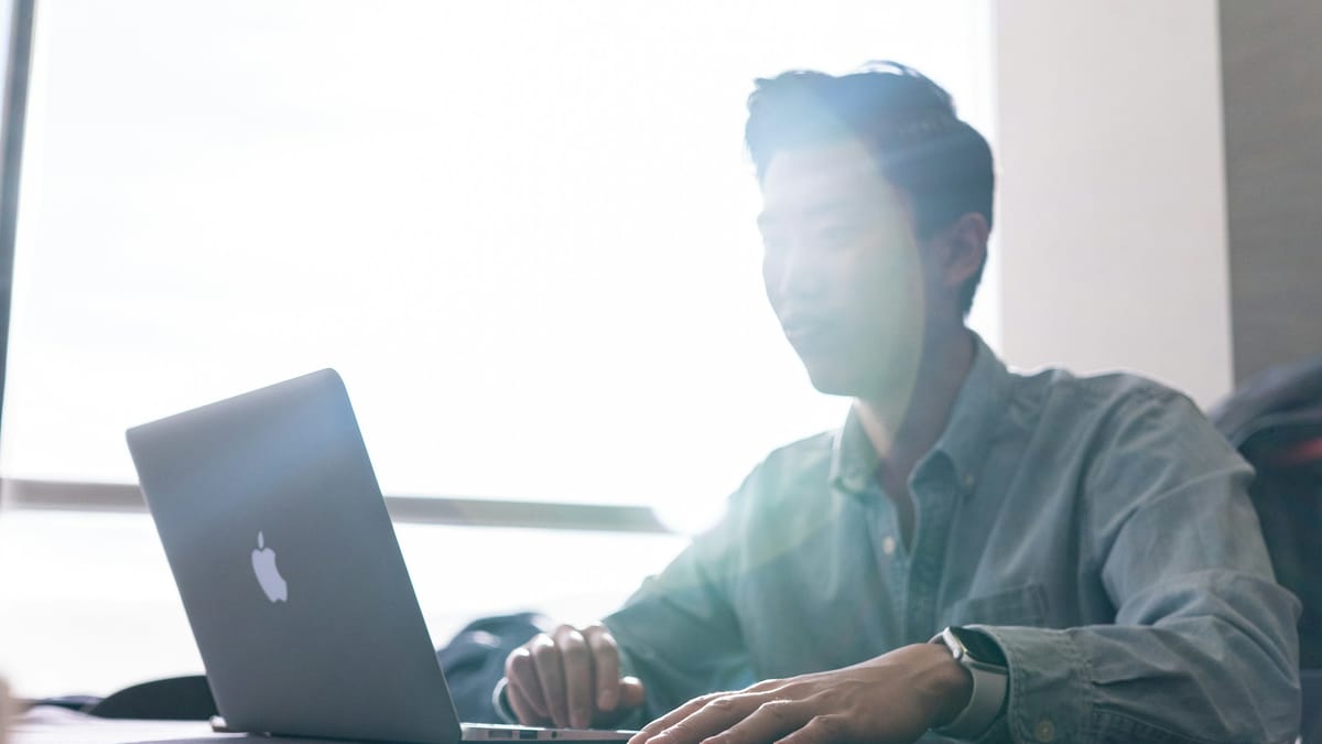 A man working on a laptop at a bright desk by a window