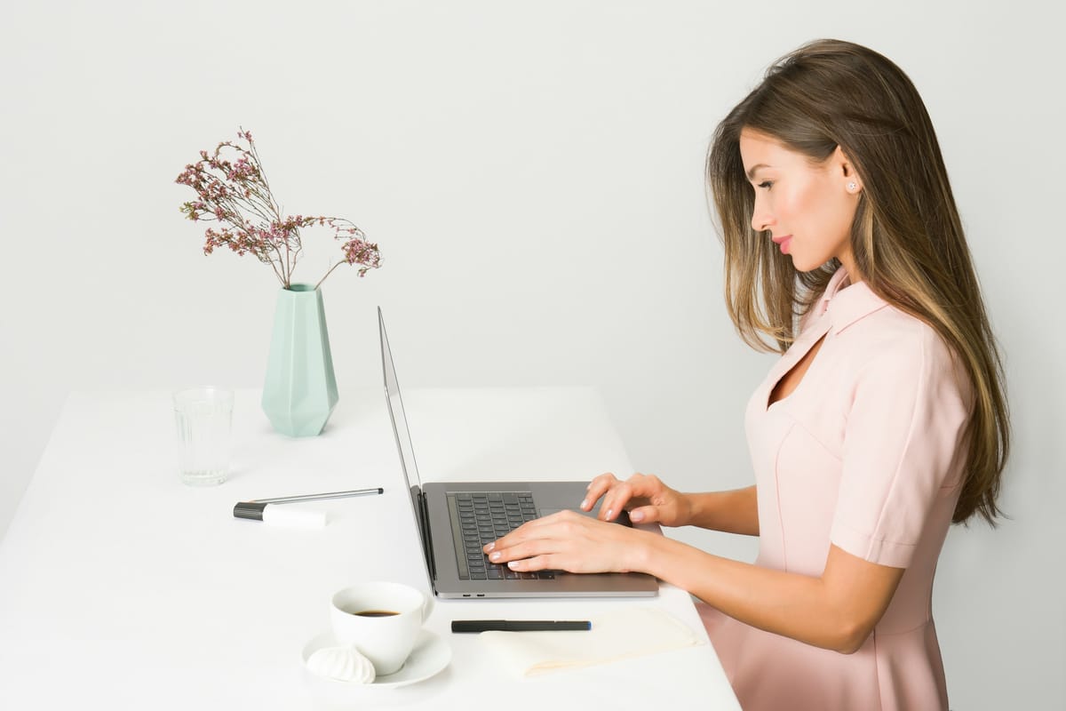 A woman sitting tall at a bright white desk, typing on a laptop