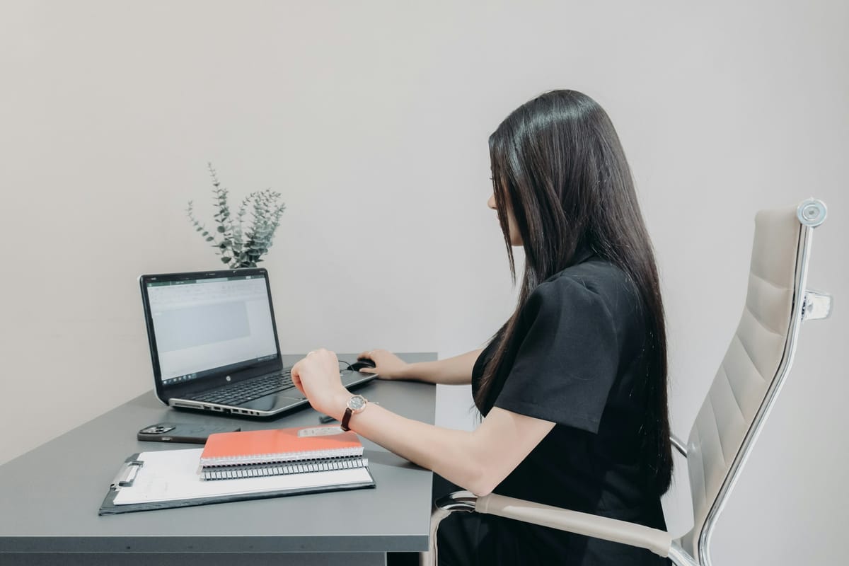 A woman leaning in toward her laptop while she works at a white desk